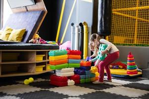 Two sisters playing at kids play center while build with colored plastic blocks. photo