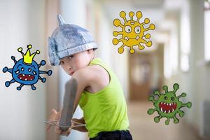 A little boy stays at home with a sword to protect against the coronavirus virus. Fight the coronavirus epidemic. A child is fighting a caricature of a virus. photo