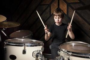 A boy is playing with a drumstick. The child behind the drum kit. photo