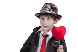 gracioso niño en un rojo Corbata y sombrero sostiene un varita mágica con un corazón. chico con un enamorado. foto