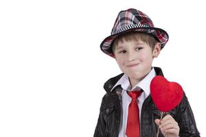 Funny child in a red tie and hat holds a wand with a heart. Boy with a Valentine. photo