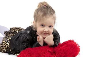 Beautiful little girl on a white background. Child blonde lies on a red pillow. Five year old blue-eyed girl. photo
