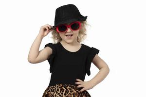 Funny child. Little girl in a black hat and sunglasses on a white background. Portrait of a beautiful fashionable baby girl. Four year old baby blonde. photo