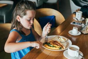 pequeño y linda chico teniendo desayuno en cafetería. comiendo tortilla con Espinacas foto