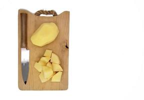 cortado en cubitos pelado patatas y todo pelado papas, en un de madera corte junta, y un cocina cuchillo. foto
