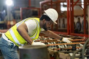 trabajador industrial afroamericano está comprobando el valor de configuración de la máquina formadora de rollos de chapa dentro de la fábrica de techos para el concepto de construcción de la industria de seguridad foto