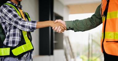 Construction team shake hands greeting start new project plan behind yellow helmet on desk in office center to consults about their building project. photo