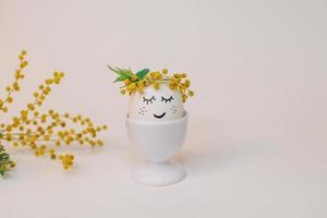 un blanco huevo con un cara hecho de flores se sienta en un huevo cáscara con un amarillo flor en él. foto