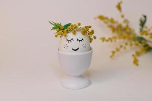 A white egg with a face made of flowers sits in an egg shell with a yellow flower on it. photo