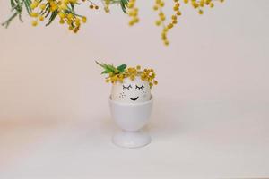 A white egg with a face made of flowers sits in an egg shell with a yellow flower on it. photo