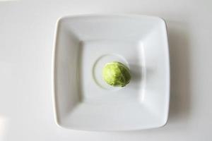 small green brussels sprouts on a white plate on a white isolated background photo