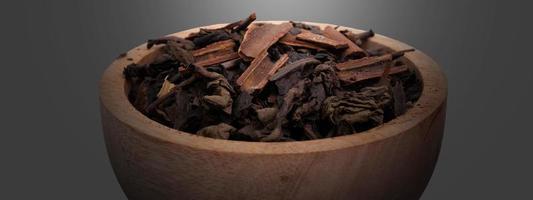 seco fermentado té hojas con canela en un de madera cuenco en un oscuro antecedentes foto