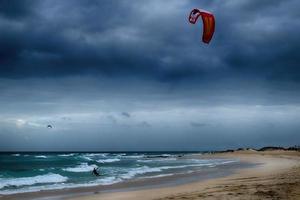 summer landscape with the ocean with dark cloudy waves and surfermi kit with parachutes floating on the shore photo