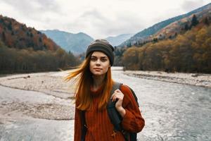 beautiful woman in a sweater with a backpack in the mountains near the river in nature portrait photo