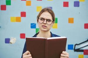 sorprendido hembra estudiante en lentes en el calle con un libro de emociones modelo foto