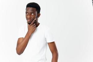 puzzled african man looking to the side touches his face with his hand on a light background photo