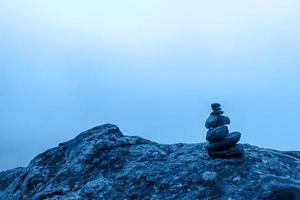 Minimalism. A small cairn stands on a large boulder with dense fog in the background. Blue tinting in color 2020. Horizontal. photo