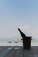 Wine bottle with two glasses on wooden deck by the lake. photo