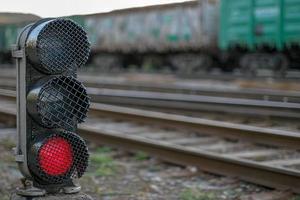 Semaphore with a glowing red lamp close-up. Selective focus on the semaphore. Background with rails and wagons blurred. photo