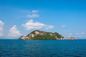 Rocky island in the sea against the blue sky with clouds. A lot of green trees on the slopes. The weather is sunny. Horizontal. photo