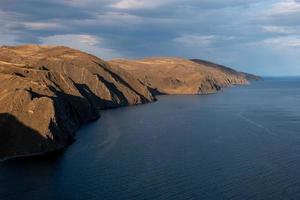 Incredible views of the rocky shore of Lake Baikal. Brown cliffs. There are ripples on the lake. Clouds in the sky. photo