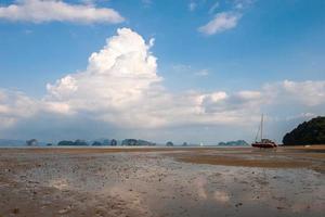 Low tide at sea with rocks on the horizon and a catamaran in the sand without water. Beautiful clouds on the blue sky. Horizontal. photo