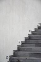 The staircase on the white wall of the building in the park, the gray stone staircase on the white cement wall background. photo