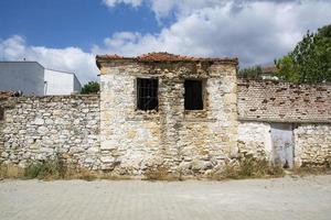 The window of an old stone house with a broken window in the foreground, ruins of an old house in the village. photo