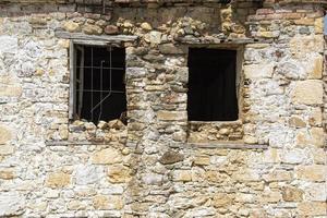 The window of an old stone house with a broken window in the foreground, ruins of an old house in the village. photo