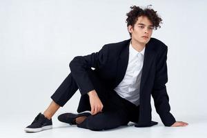 de moda chico en un traje y zapatillas sentado en el piso en un brillante habitación Rizado pelo modelo foto