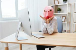 Cute crazy businesswoman worker freelancer in pink fish mask work on computer online pondering or making decision thinking of problem solution recline on hands in light modern office. Copy space photo