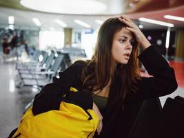 woman holding her head waiting airport yellow backpack tired photo