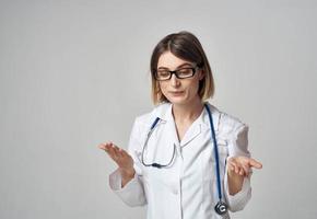 woman nurse in a medical gown gesturing with her hands on a light background copy space photo