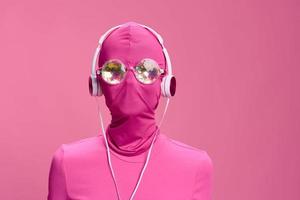 Creative fan art photo of a young female cyberpunk blogger on a pink background wearing a pink full-face mask with glowing round glasses and headphones