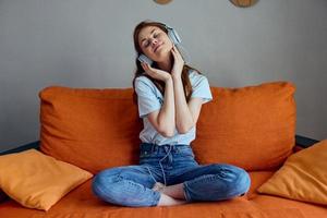 bonito mujer sentado en el sofá a hogar escuchando a música en auriculares apartamentos foto