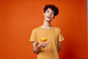 alegre Rizado chico en un amarillo camiseta naranjas en su manos rojo antecedentes foto