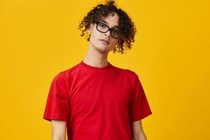 Lovely myopic young student man in red t-shirt funny eyewear looks at camera posing isolated on over yellow studio background. The best offer with free place for advertising. Education College concept photo