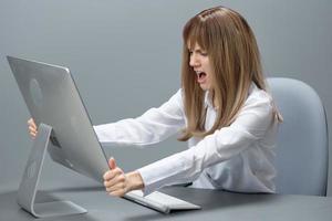 Angry evil pretty blonde businesswoman screaming to desktop Raging after computer software crash error sitting at workplace in gray modern office. Technology And Operation Problem Concept. Copy space photo