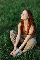 A young woman in summer clothes sitting on the green grass doing yoga and meditating in nature, a connection with the cosmos. The concept of harmony with body and nature, spiritual growth photo