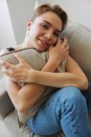 joven mujer con corto Corte de pelo pelo teniendo divertido a hogar en el sofá sonrisa y felicidad, vacaciones a hogar, natural posando sin filtros, gratis Copiar espacio foto