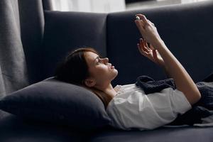 a woman lies on a gray sofa with a mobile phone in her hand side view photo