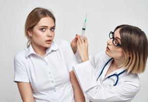 Female doctor shows the patient a syringe and a medical gown a stethoscope photo