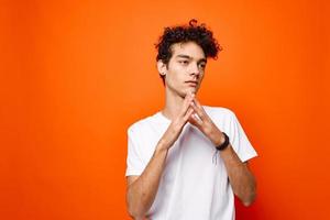 curly guy in a white t-shirt gesturing with his hand on an orange background photo