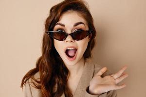 woman in glasses with open mouth and gesturing with hands beige background photo