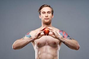 male athlete with an apple in his hands and tattoo cubes on his stomach biceps press photo