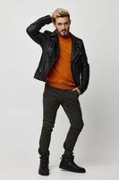 elegante hombre en naranja suéter cuero chaqueta pantalones modelo rubio foto