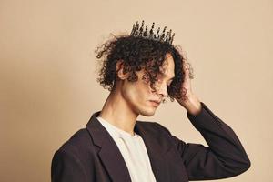 Pretty cute handsome funny narcissistic tanned curly man with crown posing isolated on over beige pastel background. Fashion New Collection offer. Retro style concept. Free place for ad photo