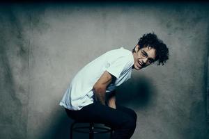 cute guy in a white t-shirt sits on a chair emotions curly hair photo