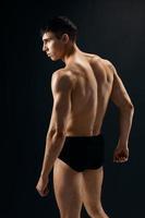 a handsome man bodybuilder with a pumped-up body stands with his back dark background photo