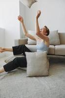 Teenage girl smile everyone sits at home near the couch and tosses up pillows, fun game and happiness without filters, copy place photo